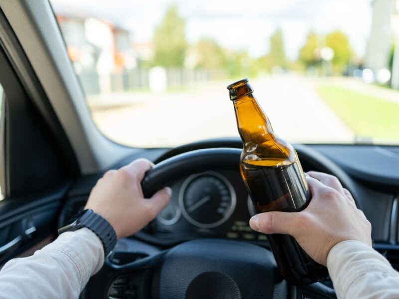 A man is holding a bottle of beer while he operates a motor vehicle.