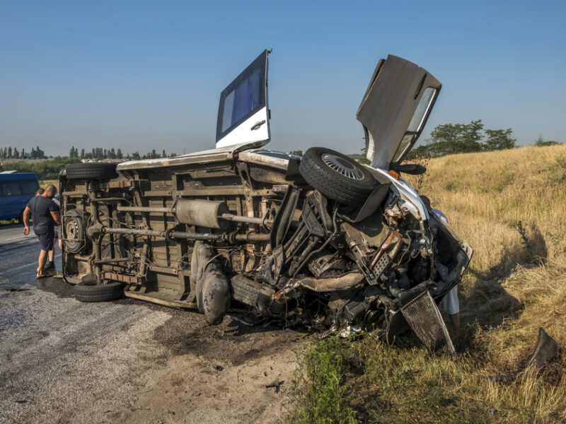 A shuttle bus is turned over after a crash on the side of the road.